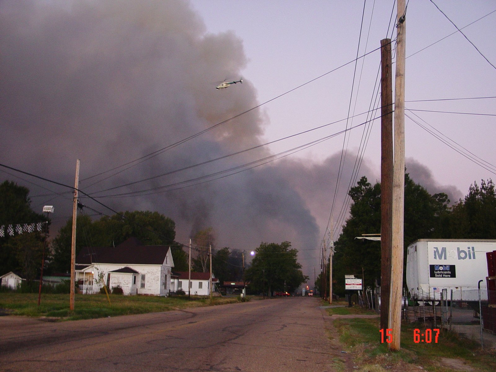 Smoke clouds visible from far away, helicopter flies overhead.